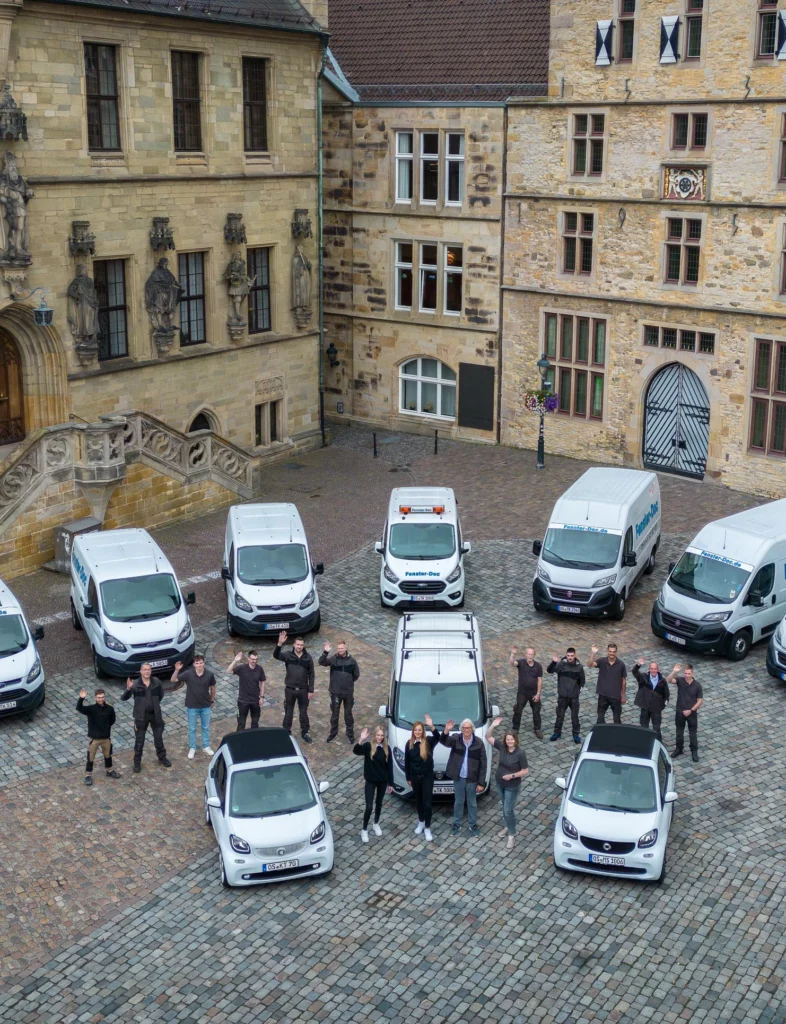 Historisches Gebäude mit Sandsteinfassade, davor weiße Fahrzeuge und eine winkende Gruppe in dunkler Kleidung.