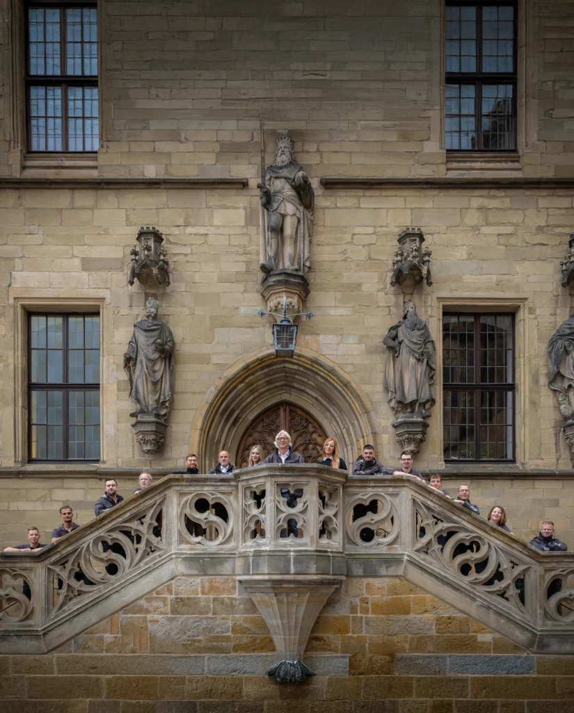 Menschen auf verziertem Balkon eines historischen Gebäudes posieren für ein Gruppenfoto.