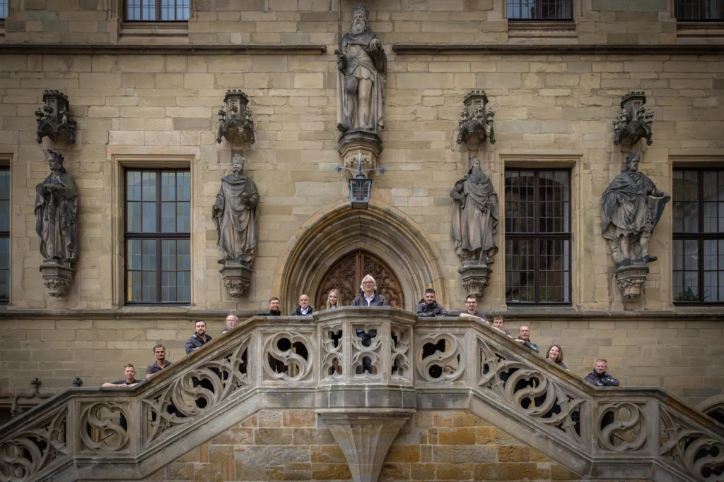 Eine Gruppe posiert auf einer Treppe vor einem historischen Gebäude mit geschnitzter Fassade.